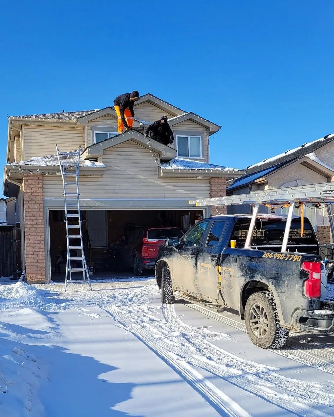 Jet Set crew on the roof of a Winnipeg two-storey home hanging Christmas lights, ladder and truck in the snowy driveway