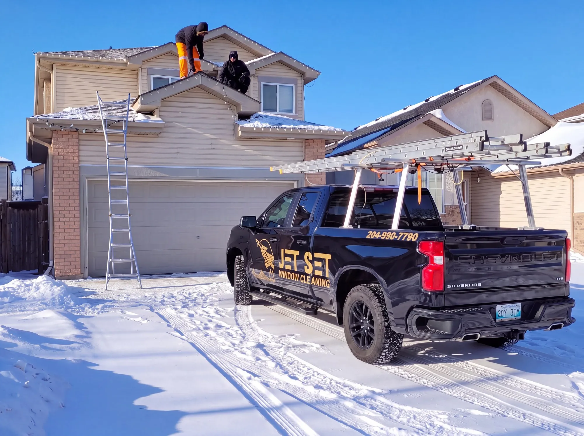 Jet Set crew clipping Christmas lights along a Winnipeg two-storey roofline, ladder up and the Jet Set truck in the driveway