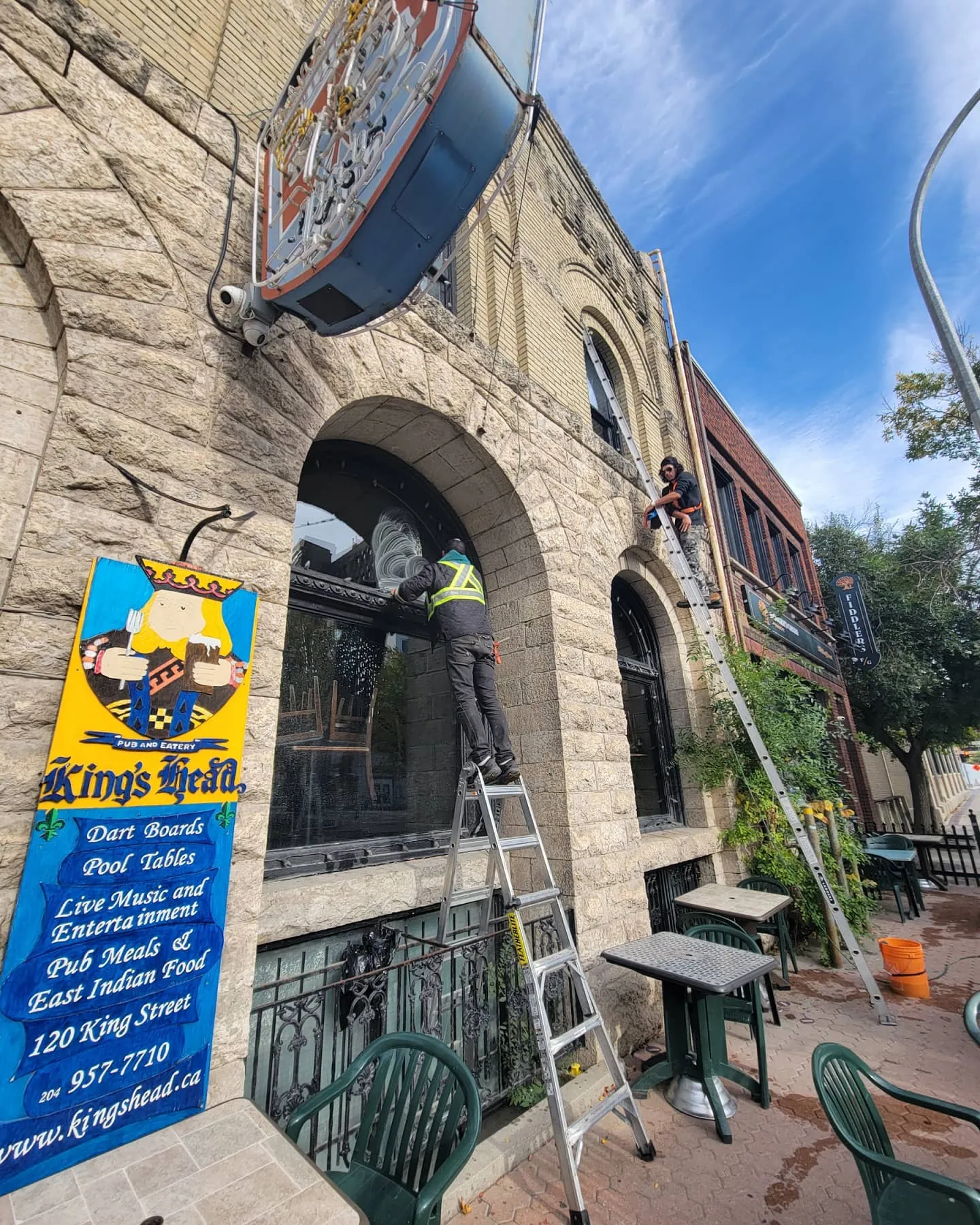 Technician on a ladder cleaning the arched windows of a heritage brick pub in Winnipeg