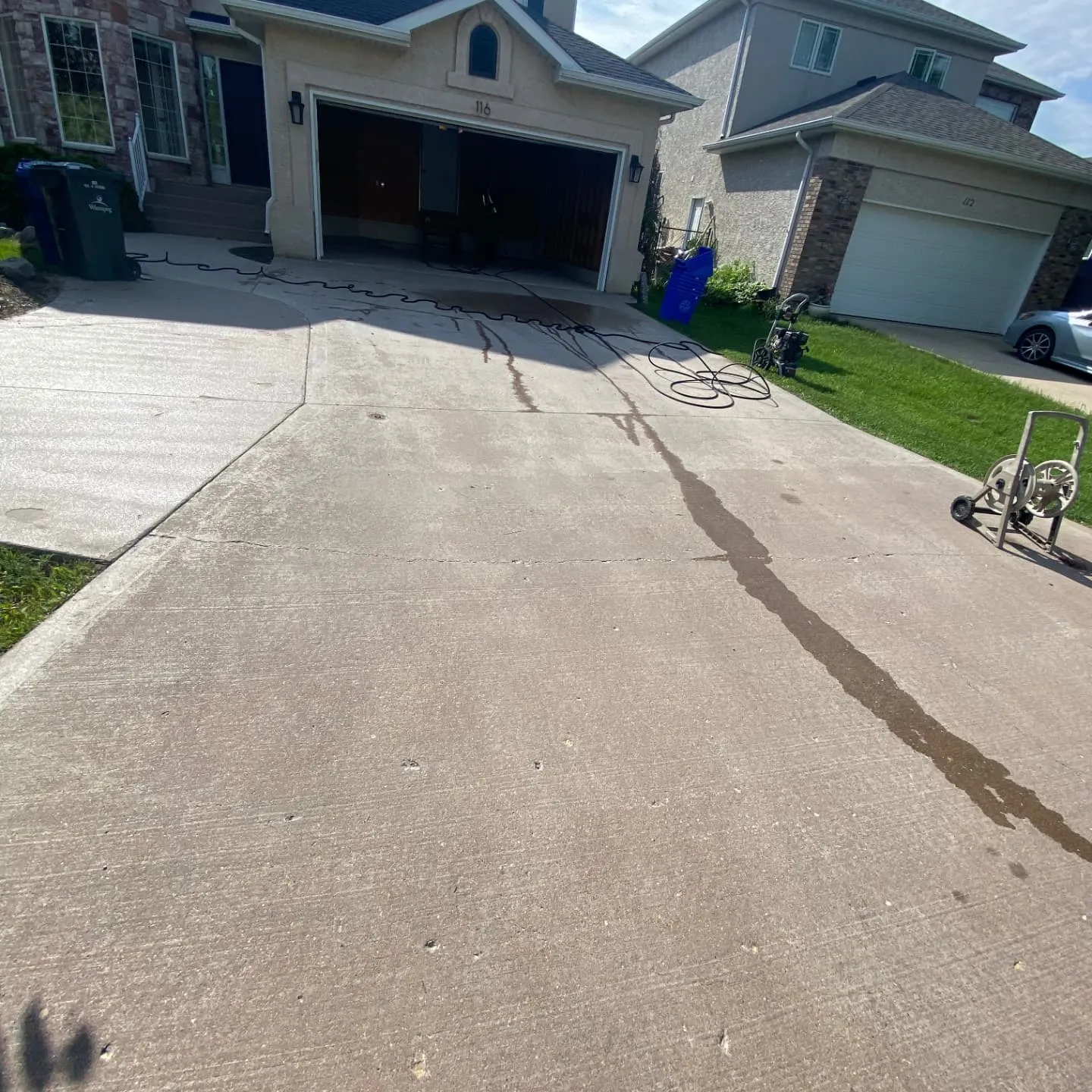 Concrete driveway in Winnipeg being pressure washed, with the cleaned strip showing against the grey