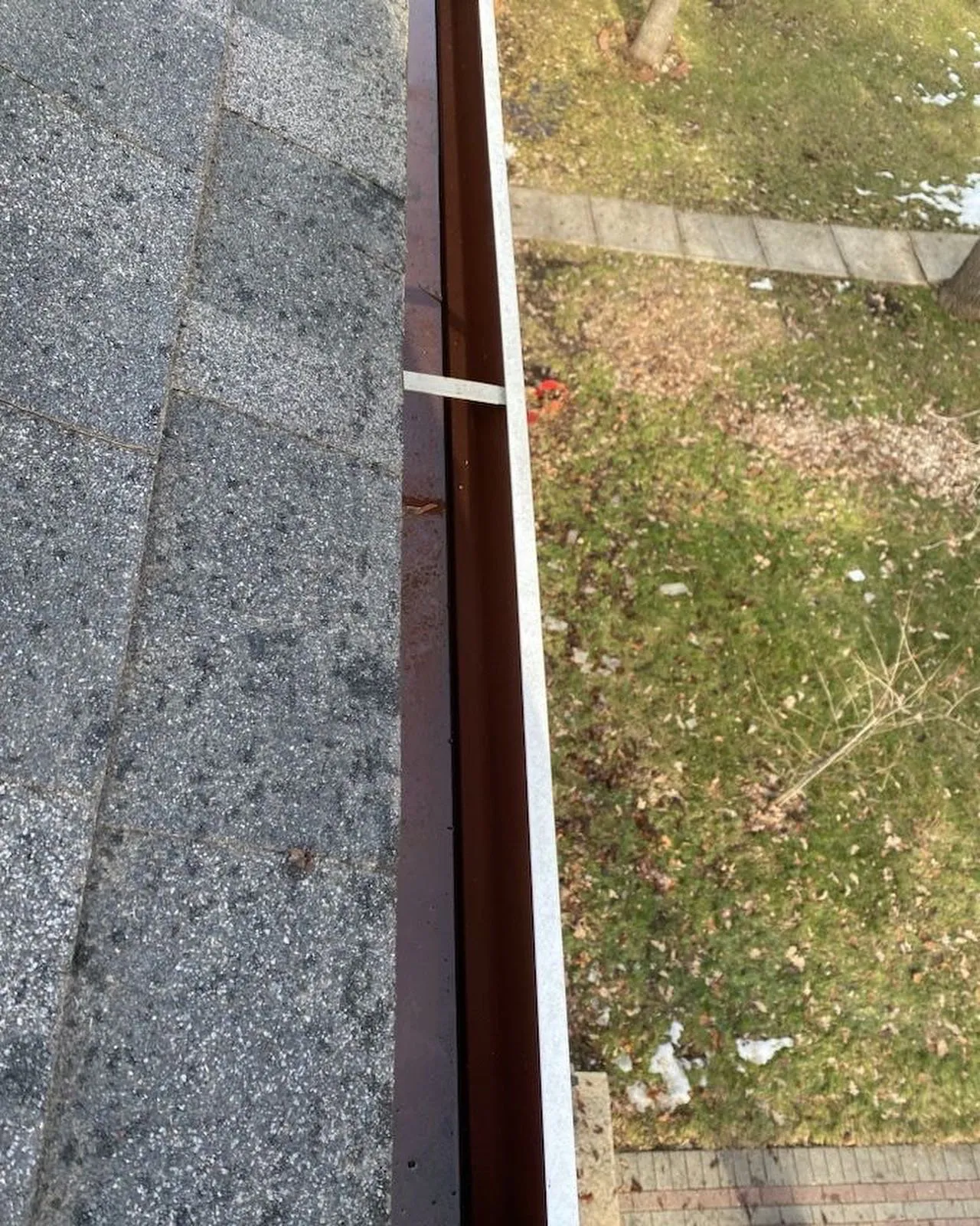Clean brown eavestrough along a shingle roof after cleaning in Winnipeg