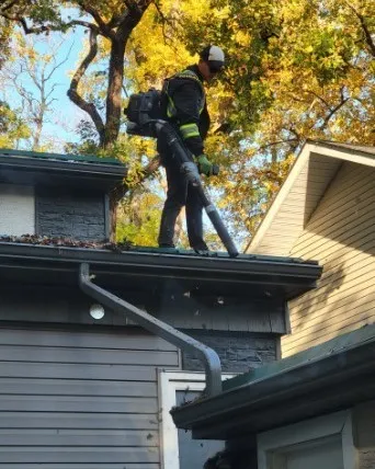 Jet Set technician at the roof edge clearing a leaf-filled eavestrough under autumn trees in Winnipeg