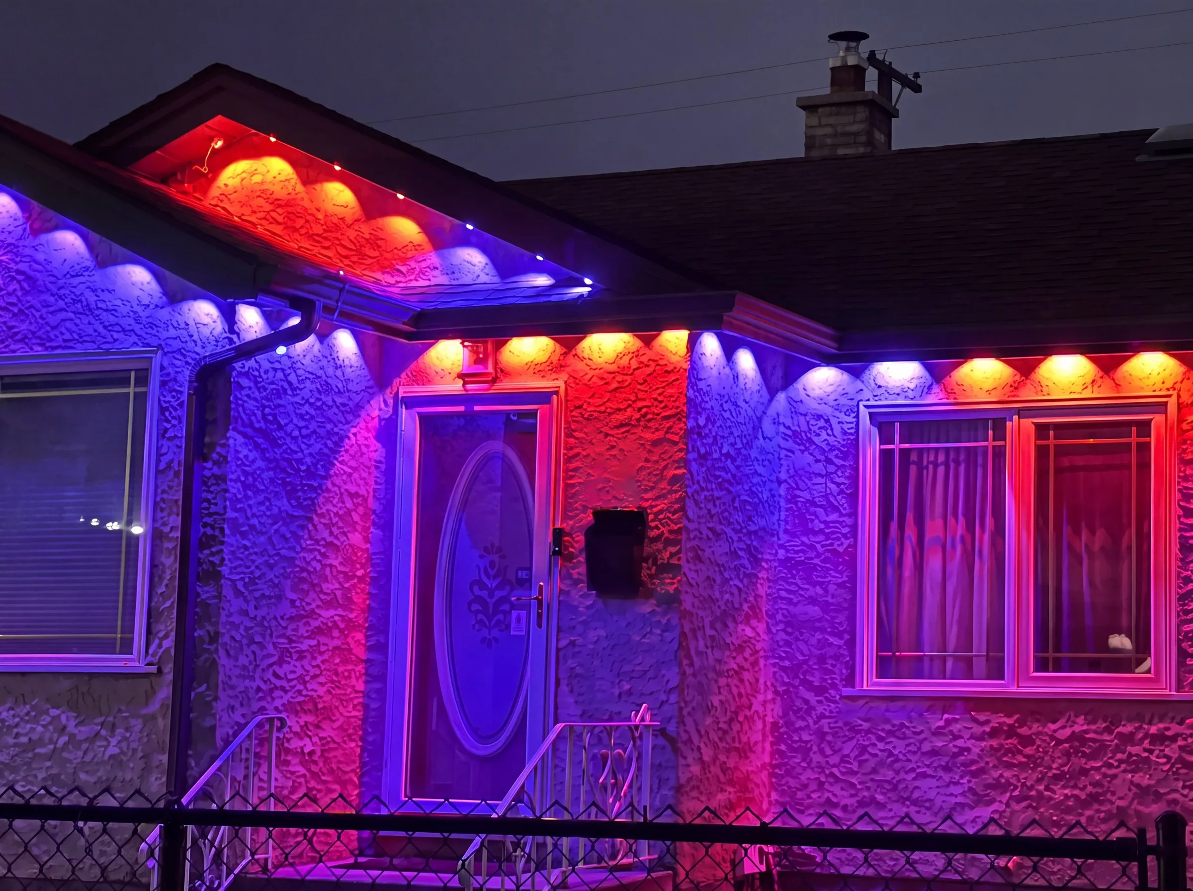Winnipeg stucco bungalow entry with Govee permanent lights in blue-purple, red and orange blocks along the eaves