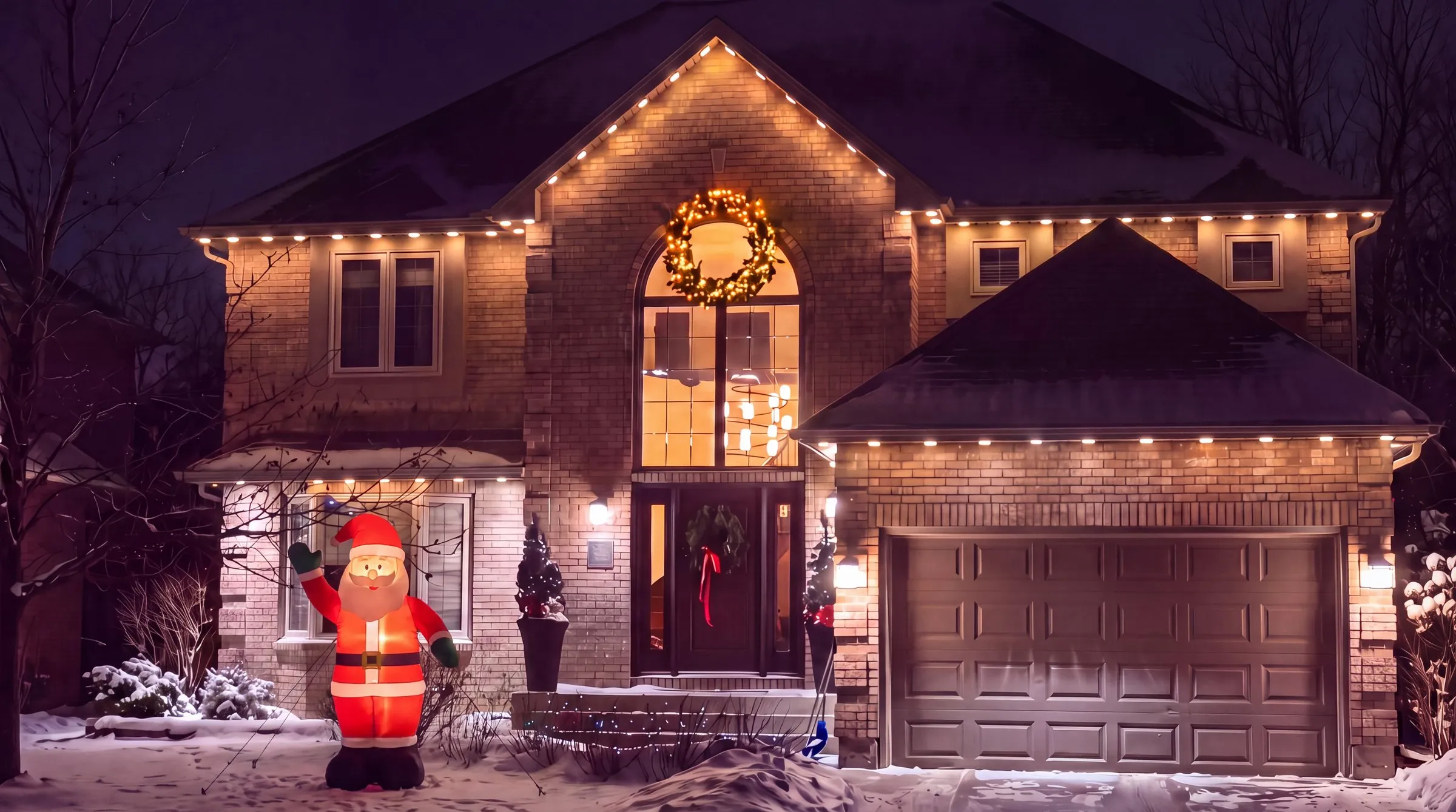 Winnipeg brick home at night with an eight-foot inflatable Santa glowing on the front lawn and warm white Govee lights along the roofline