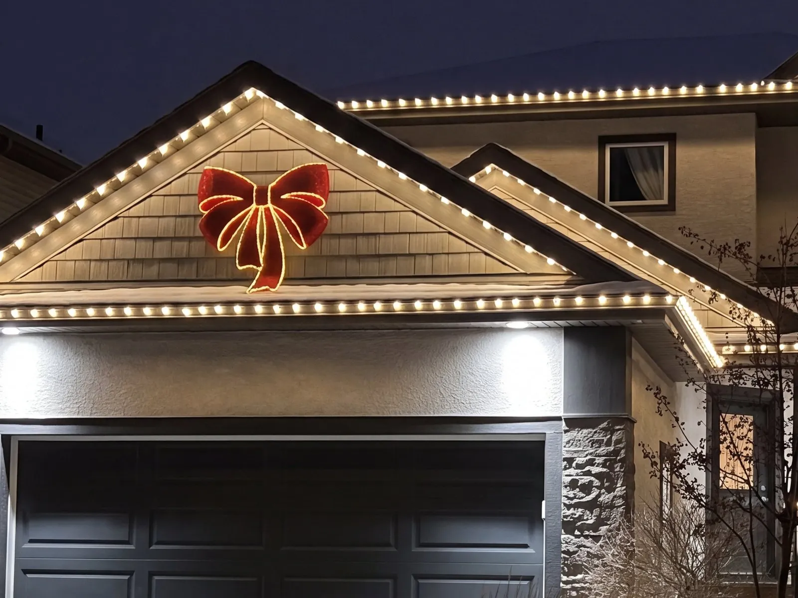 Lit red bow mounted on the gable above a Winnipeg garage, with Govee lights along the eaves