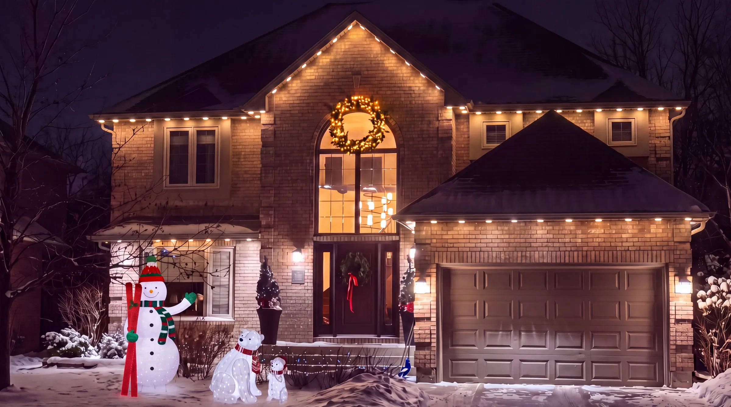 Winnipeg brick two-storey home at night with a lit snowman and two lit polar bears on the snowy front lawn, warm white Govee permanent lights along the roofline and a lit wreath in the arched window