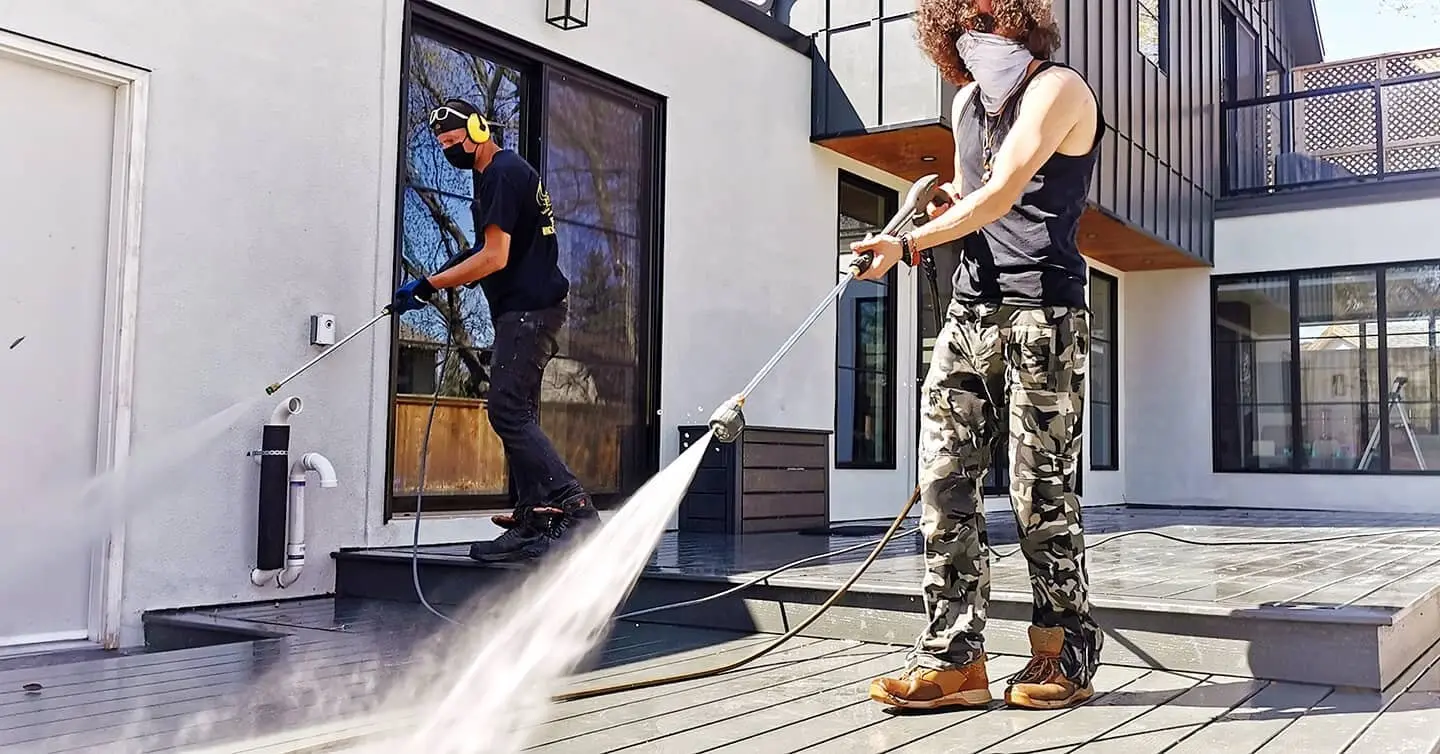 Two technicians pressure washing the entrance steps and walls of a modern home