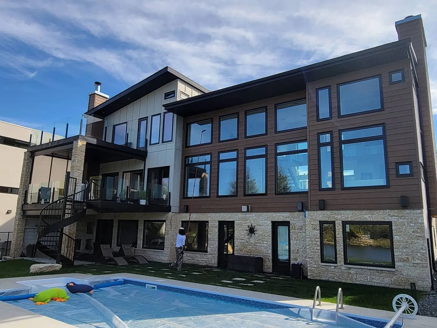 Technician cleaning the windows of a three-storey stone and cedar home from the pool deck in Winnipeg