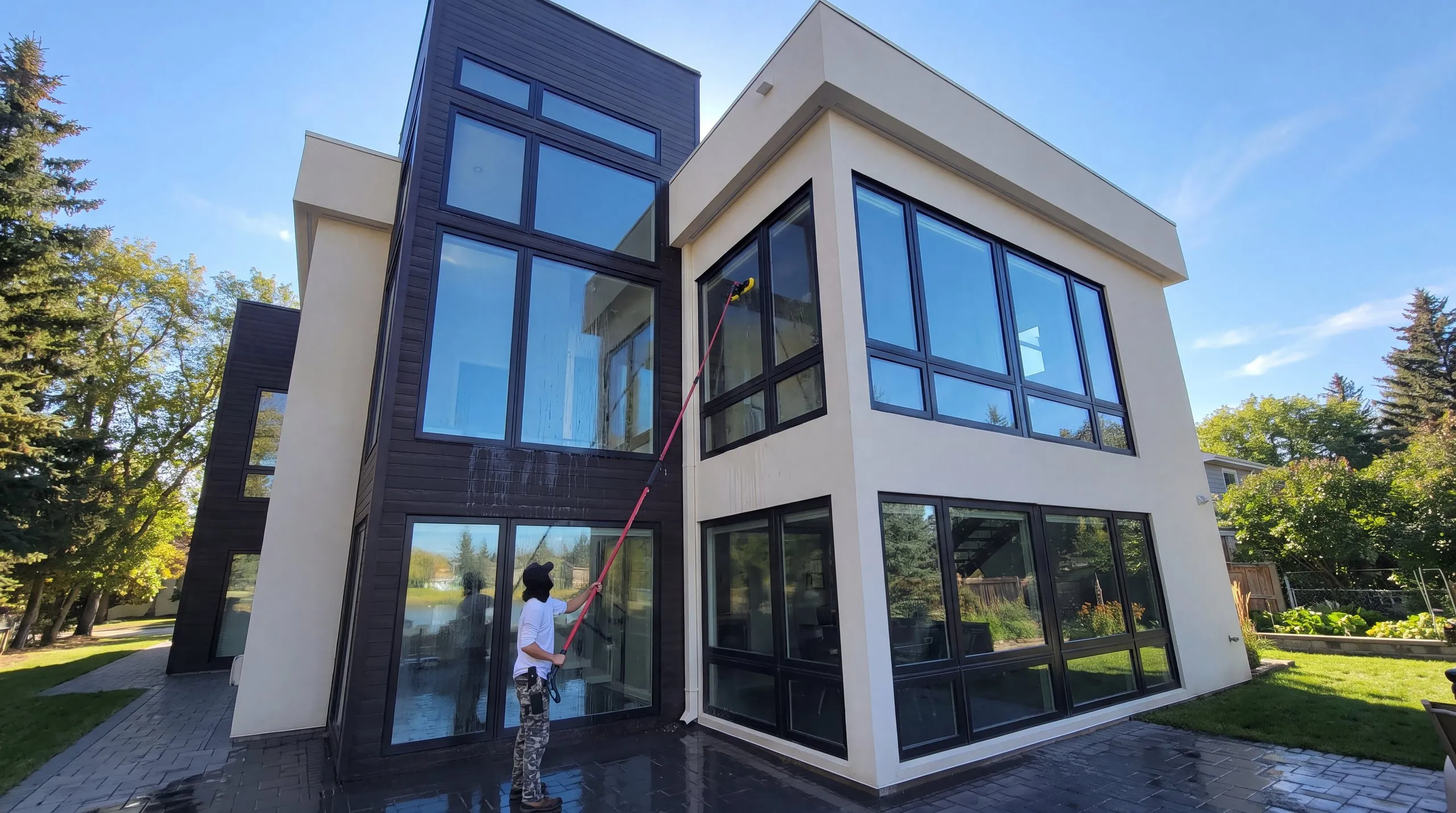 Jet Set technician washing the tall windows of a modern Winnipeg home from the ground with a water-fed pole on a sunny day